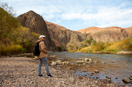 a female tourist stands on the bank of a mountain river in a mountain gorge with ancient trees and a blue bright skyの写真素材