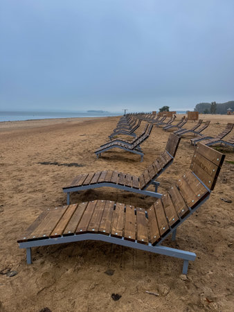 Empty wooden loungers on a sandy lakeside beach in early summer, calm and ready for the season to beginの写真素材