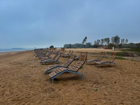 Empty wooden loungers on a sandy lakeside beach, peaceful scene marking the quiet end of the holiday seasonの写真素材