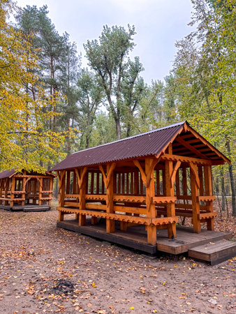 Wooden picnic gazebo in a park surrounded by greenery, offering shade and seating for outdoor relaxation and leisureの写真素材
