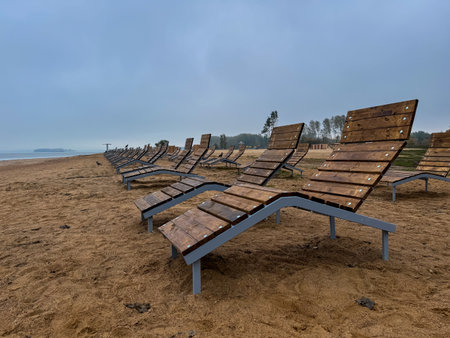 Empty wooden loungers on a sandy lakeside beach, peaceful scene marking the quiet end of the holiday seasonの写真素材
