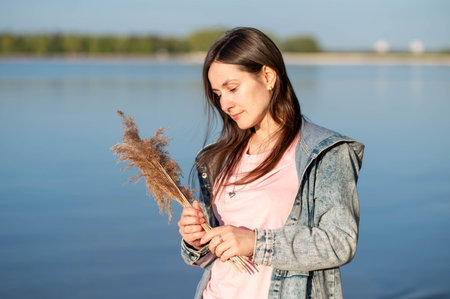 Woman embracing nature by a lake, holding dried blooms and savoring the warmth of the sunの写真素材