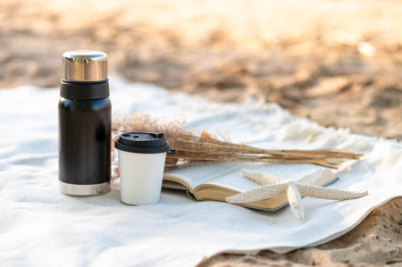 On a white blanket on the sand: thermos, hot drink, book, dried flowers, and starfish, boho style.の写真素材