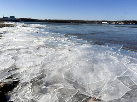 Cracked ice on a rocky shore of a thawed lake under a bright spring blue sky. A contrast of melting...