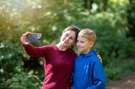 Mother and son making funny faces while taking a selfie during a spring forest walk, enjoying playful family time in natureの写真素材