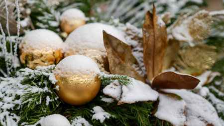 Snow-covered golden Christmas ornaments resting on evergreen branches, creating an elegant festive winter holiday atmosphere with soft sparkle and seasonal charmの写真素材