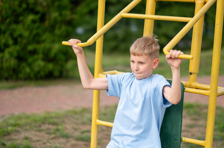 Focused teenage boy uses outdoor gym equipment to build strength and stay fit on a warm summer day...