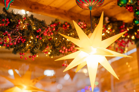 Large glowing Christmas star hanging among festive garlands with red berries and warm lights,...