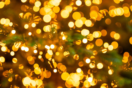 Soft glowing golden Christmas lights forming a bright festive bokeh on lush evergreen branches,...