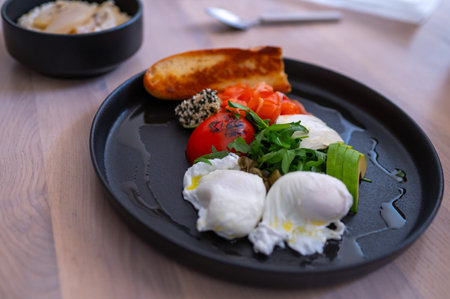 Breakfast with poached eggs, vegetables, toast and sauce served on black plate