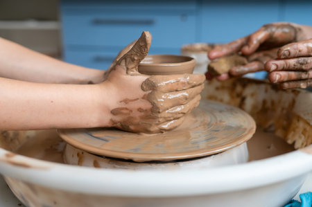Child and adult hands molding clay together, creating a ceramic cup on pottery wheel, close-up teamworkの写真素材