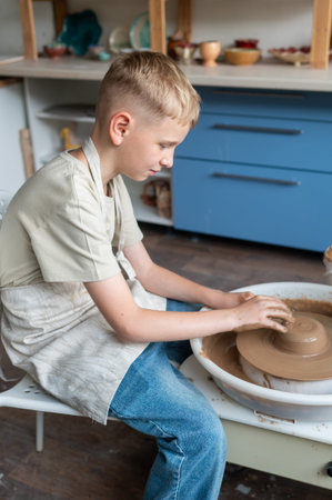 Blond boy learning pottery, close-up of hands shaping clay on a wheel, creative kids activity in cozy pottery studio, teamwork and manual craft skills conceptの写真素材