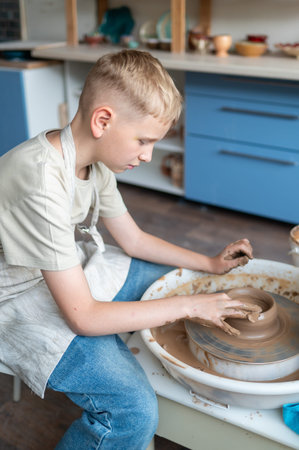 Blond boy learning pottery, close-up of hands shaping clay on a wheel, creative kids activity in...