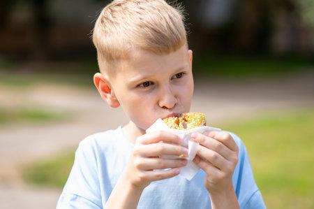 Smiling teen boy enjoying a sweet donut outside on a warm sunny day, savoring the treat and having...