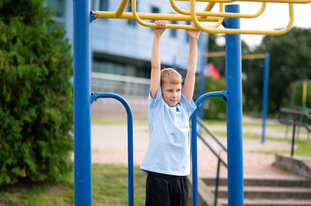Focused blond boy hangs on horizontal bars during outdoor workout, building strength and having fun...