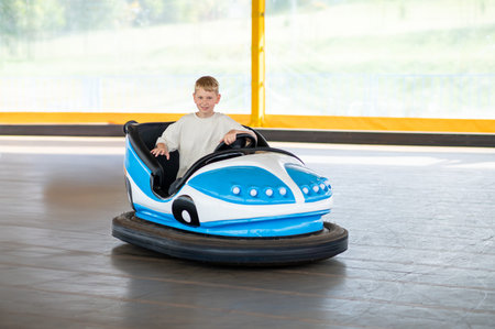 Blond teenage boy enjoying electric bumper car ride at amusement park, laughing and having fun, concept of childhood, leisure and summer activitiesの写真素材