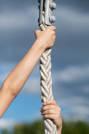 Close up of teenage boy hands gripping rope outdoors with clear blue sky background, concept of...