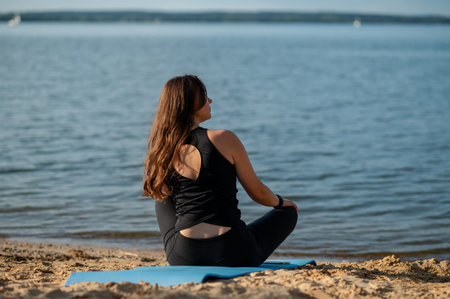 Woman sits on the shore of a lake, looking into the distance, enjoying a peaceful summer day in...