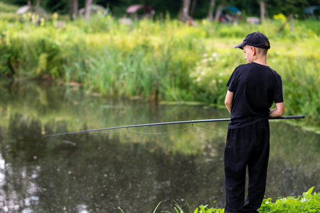 Teenage boy fishing by the calm lake, enjoying a peaceful summer day in nature, focused on catching...