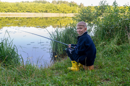 Young boy fishing by the river on a summer day, enjoying outdoor leisure and countryside atmosphereの写真素材