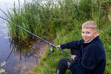 Young boy fishing by the river on a summer day, enjoying outdoor leisure and countryside atmosphere