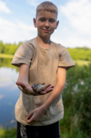 Boy proudly holding a freshly caught fish in his hand, close-up focus on the fish, outdoor fishing...