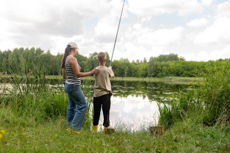 mom and teenage son fishing by the lake on a sunny summer day, bonding, relaxing outdoors, enjoying...