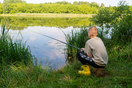 Young boy patiently fishing by river surrounded by green nature on peaceful summer day