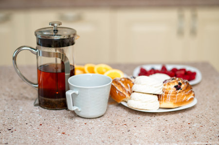Cozy kitchen scene with teapot, marshmallows, fresh buns and fruits on a countertop, warm homey...