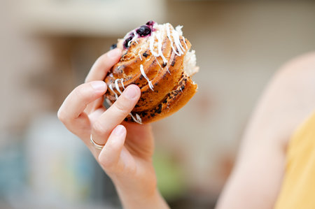 Close-up of a bitten pastry held in a woman's hand, symbolizing sweet indulgence and comfort in...