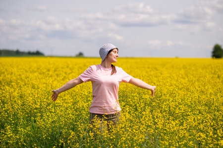 Young woman in a field of yellow flowers. Girl in a hat and pink shirt.