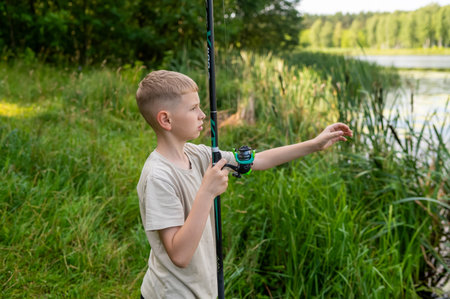 Teenager boy casting fishing rod on a sunny summer day by the lake or river, enjoying active outdoor...
