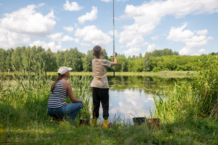 mom and teenage son fishing by the lake on a sunny summer day, bonding, relaxing outdoors, enjoying nature, peaceful water views and quality family timeの写真素材