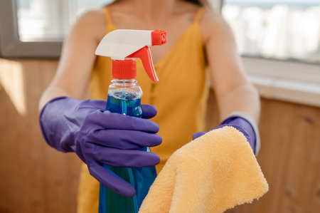 Gloved hands gripping a window cleaning spray bottle and cloth, ready for cleaning tasks and...