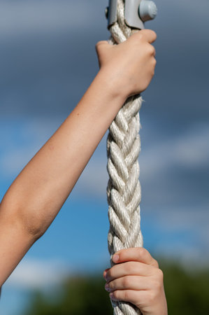 Close up of teenage boy hands gripping rope outdoors with clear blue sky background, concept of...