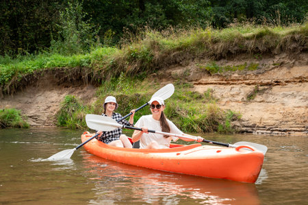 Two happy young women kayaking on river, enjoying friendship, outdoor activity, and summer adventure...