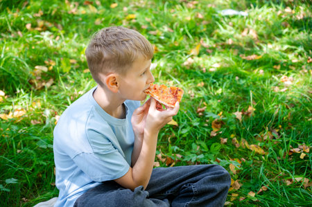 Blond teenage boy enjoying slice of pizza at summer picnic, outdoor leisure activity with tasty fast food, casual lifestyle scene in green park nature environmentの写真素材