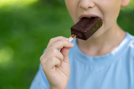 Close up of boy biting chocolate ice cream on a stick, concept of summer dessert, sweet snack and...