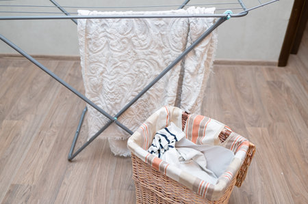 Laundry drying on rack with wicker basket of clothes next to it, concept of home chores, cleaning,...