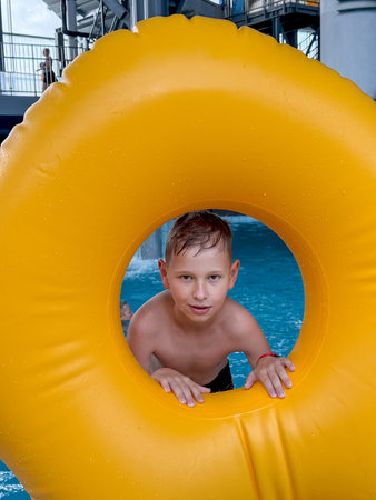Smiling boy having fun in an indoor water park, holding a giant inflatable float, enjoying...