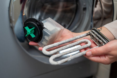 A person holds a limescale-covered heating element and a washing machine drain pump during repair and maintenance, showing appliance care and cleaning processの写真素材