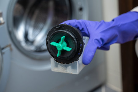 Close-up of a person wearing purple gloves holding a washing machine drain pump motor with a green...