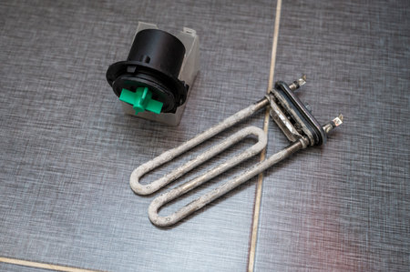Used washing machine heating element covered with limescale and a pump motor with green impeller lie...