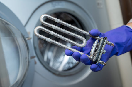 Person wearing purple cleaning gloves holds a used washing machine heating element covered with...