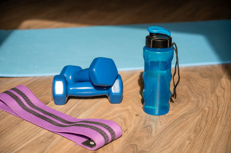 Dumbbells resistance band and water bottle placed on yoga mat on the floor at home, concept of...