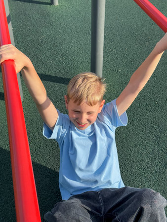 Teen boy exercising on pull-up bars at an outdoor sports playground on a sunny summer day, fitness...