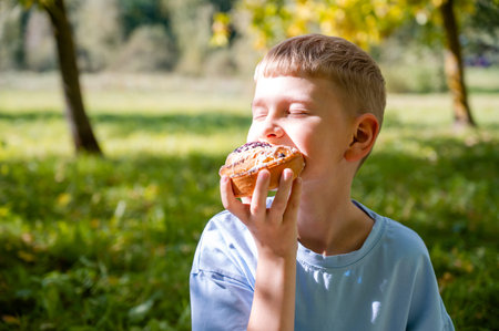 teenage boy enjoying a cinnamon roll while sitting on green grass during a summer picnicの写真素材