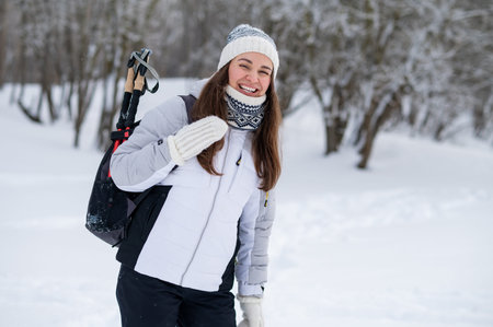 Smiling active woman carrying a backpack with nordic walking poles during a winter walk in a snowy parkの写真素材