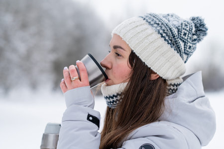 Happy woman drinking hot tea from a thermos during a winter walk in a snowy park