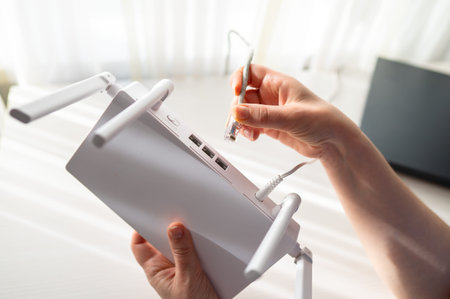 A detailed view of a person connecting a network lan cable into a wireless router with four antennas. Concept of high speed internet setup, technical support and home network installationの写真素材